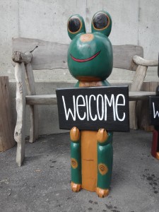 welcomeプレートを持った木彫りのカエル